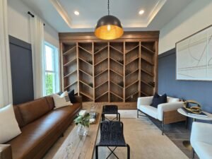 A stylish home lounge with a built-in wooden wine rack wall, a brown leather sofa, white accent chairs, black stools, and a long wooden coffee table. Soft lighting, neutral décor, and clean lines create a calm, organized space that feels comfortable and functional.