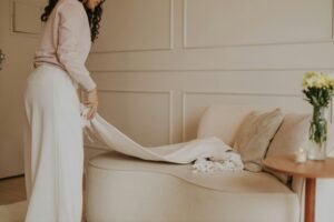 SEO Title: Simple Home Comfort Upgrades for a Better Living Space

Slug: small-home-changes-for-better-comfort

Focus Keyphrase: home comfort upgrades

Meta Description: A woman neatly arranging a light-colored throw blanket on a cozy beige sofa in a minimal, softly lit living room with neutral decor and a small table holding flowers and a candle.